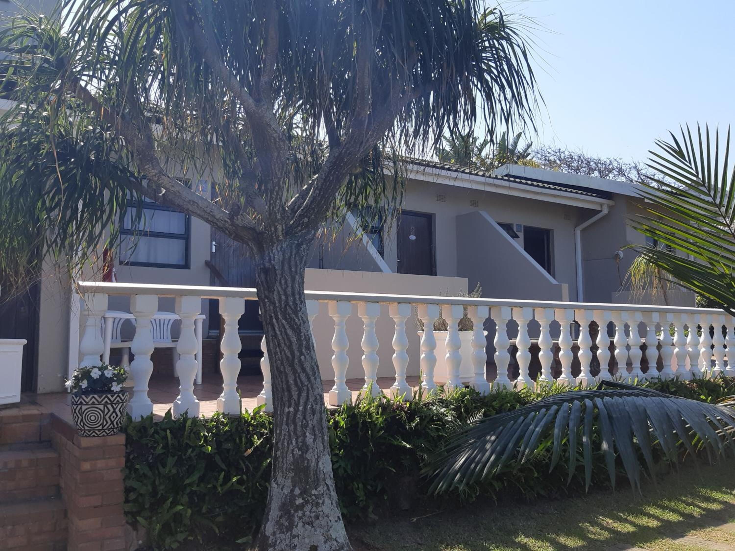 Una casa moderna con balcón blanco, rodeada de vegetación exuberante y una palmera.