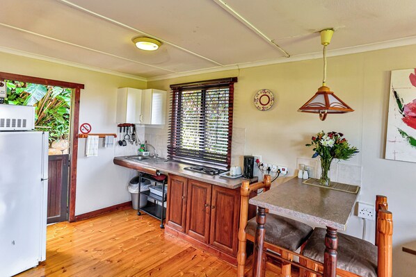 A compact kitchen with wooden cabinets, a built-in sink, and a dining area with a wooden table and chairs. - Zuider Zee Guest House (Ballito)