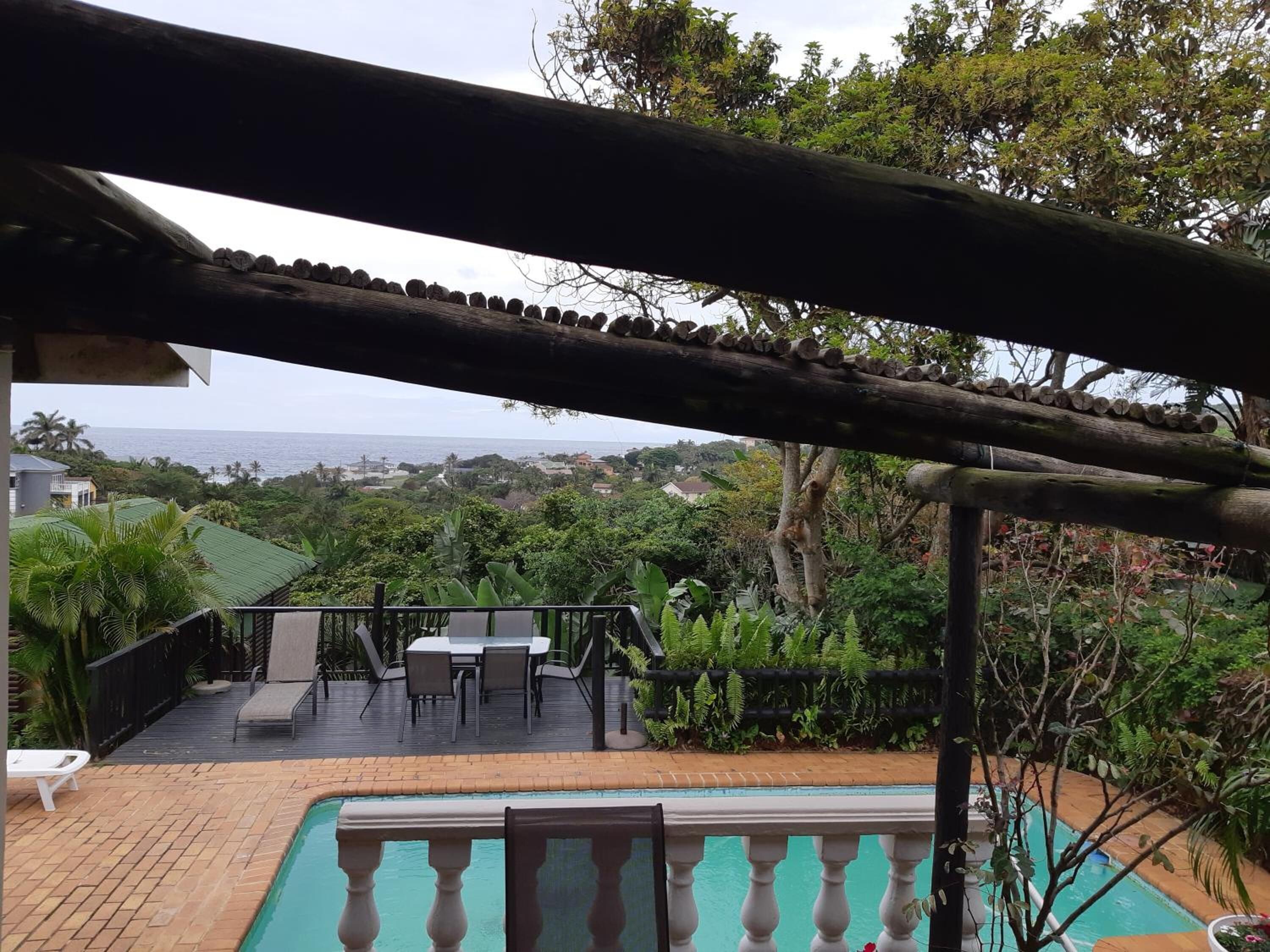 Uma área de piscina com pérgola, assentos externos e vista para o oceano.
