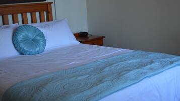 A neatly made bed with a white and teal bedspread, a wooden headboard, and a bedside table with a lamp.