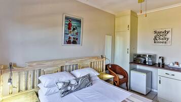 Quarto com cama, uma cadeira, escrivaninha com micro-ondas e geladeira.