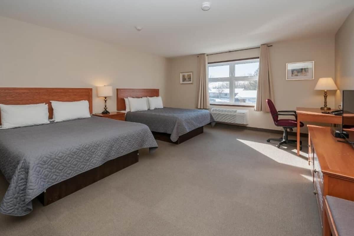 A hotel room with two beds, a desk, a chair, and a large window.
