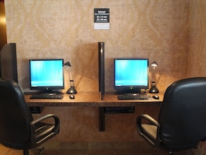 Two computer workstations with monitors, keyboards, and mice, each with a desk lamp. There are two black office chairs. A sign above the workstations indicates high-speed internet availability.
