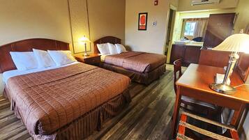 A hotel room with two beds, a desk, a chair, and a lamp.