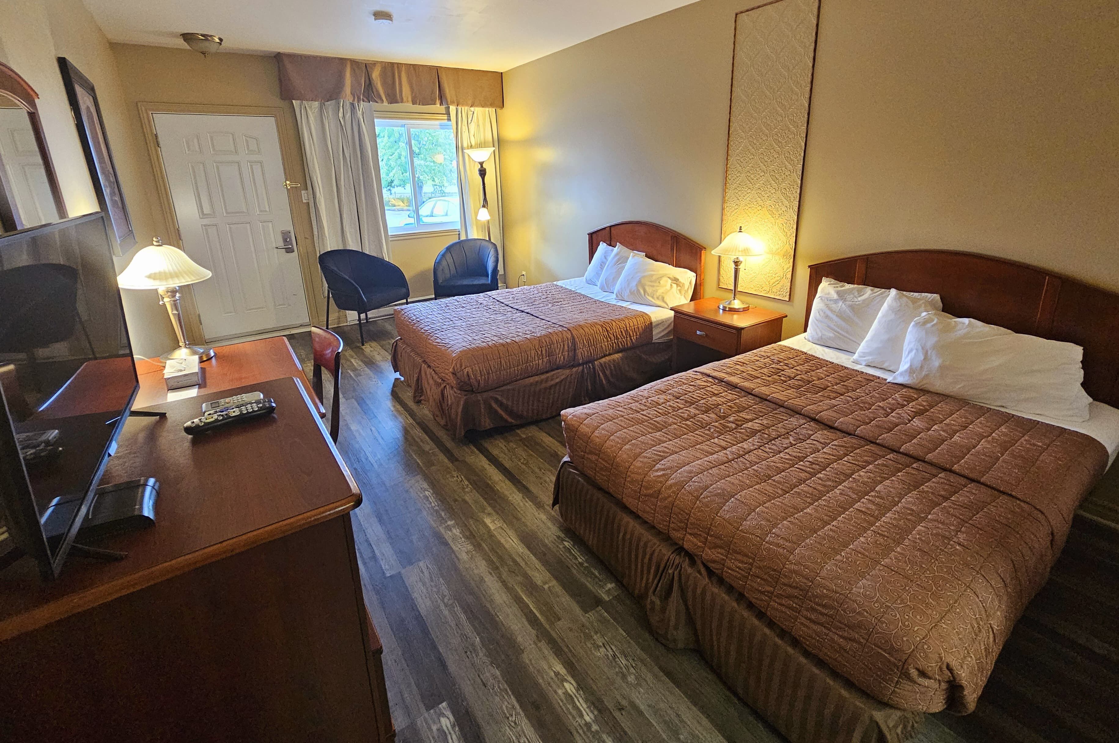 Une chambre d’hôtel avec deux lits, un bureau avec une lampe, une chaise et un téléviseur.