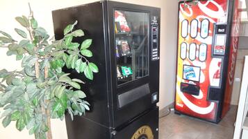 A vending machine with a Coca-Cola logo and a plant beside it.