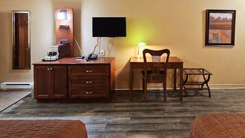 Habitación de hotel con un escritorio de madera, una silla, un televisor, una cafetera y un cuadro en la pared.