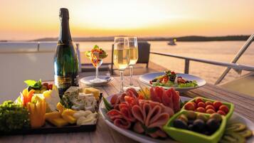 Ein Tisch mit einer Champagnerflasche, zwei Gläsern und verschiedenen Speiseplatten vor einem Sonnenuntergang.