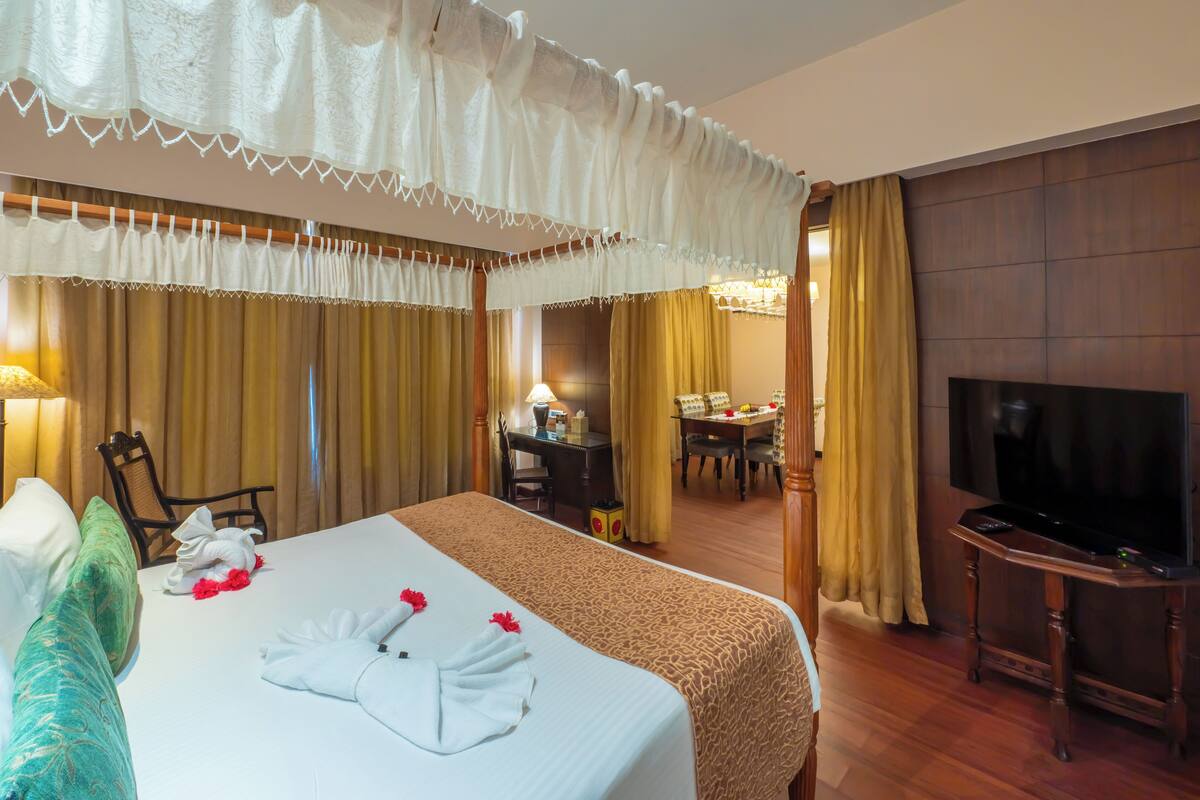 Habitación de hotel con una cama grande, televisión, escritorio con lámpara y zona de comedor con mesa y sillas.