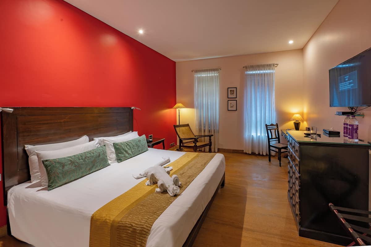 Habitación de hotel con una cama grande, un escritorio con silla, televisión y minibar.