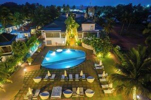 A swimming pool surrounded by lounge chairs and umbrellas, with a well-lit patio area and a view of the surrounding buildings.