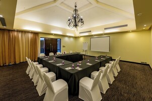 A conference room with a long table, white chairs, and a projector screen.