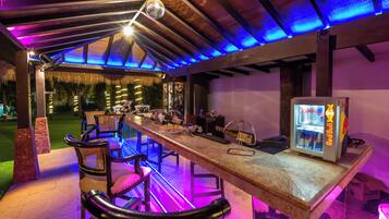 An outdoor bar area with a long wooden table, bar stools, and a Red Bull refrigerator.