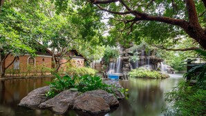 A tranquil garden with a pond, a small waterfall, and a traditional building. - Khum Phaya Resort & Spa Boutique Collection (Chiang Mai)