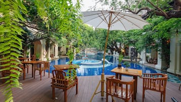 Relax by the pool surrounded by lush greenery and trees, with tables and chairs for dining and lounging.