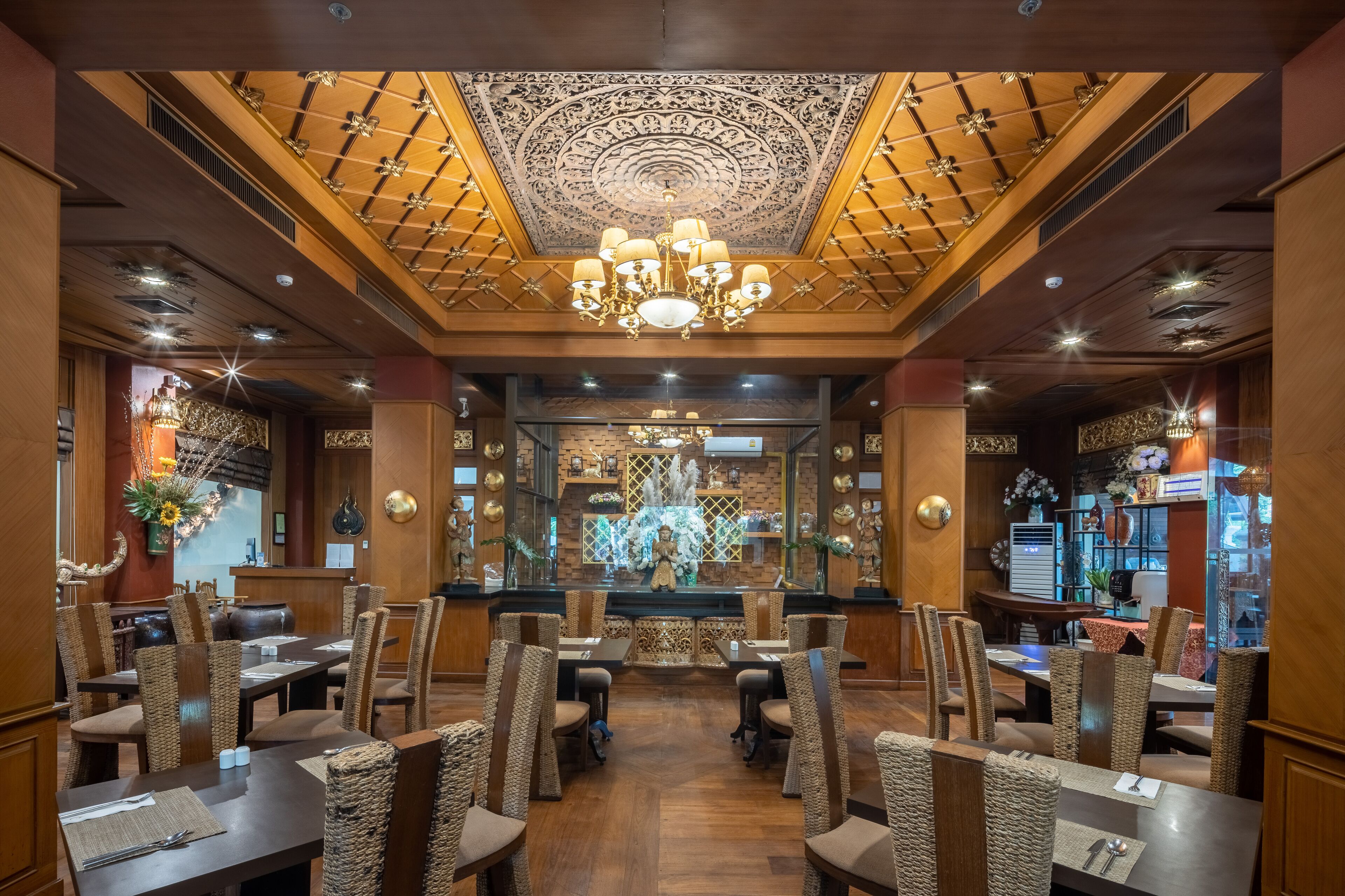 A restaurant with a central altar, wooden ceiling, and chandeliers. Tables are set with chairs, and there are decorative elements on the walls.