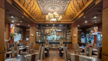 A restaurant with a central altar, wooden ceiling, and chandeliers. Tables are set with chairs, and there are decorative elements on the walls.