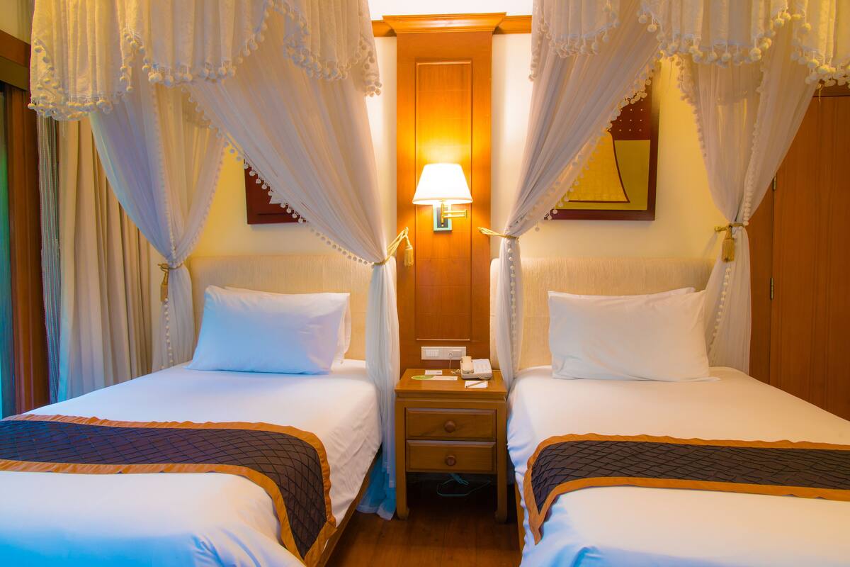 A hotel room with two beds, a nightstand with a lamp, and a wooden door.