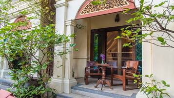 A covered outdoor seating area with wooden chairs and a table, surrounded by plants and a decorative archway.