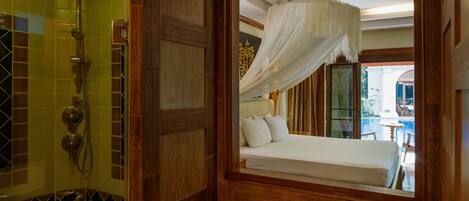 A bathroom with a shower, toilet, and a bed with a canopy.