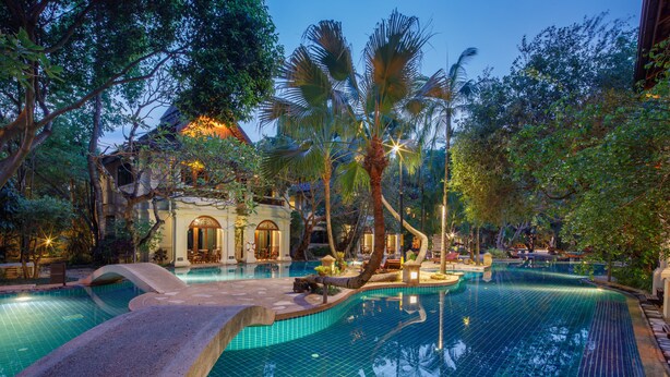 A swimming pool with a stone bridge, surrounded by lush greenery and palm trees. - Khum Phaya Resort & Spa Boutique Collection (Chiang Mai)