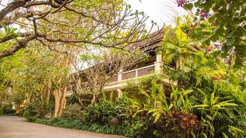 A traditional building with a balcony, surrounded by lush greenery and a paved walkway.