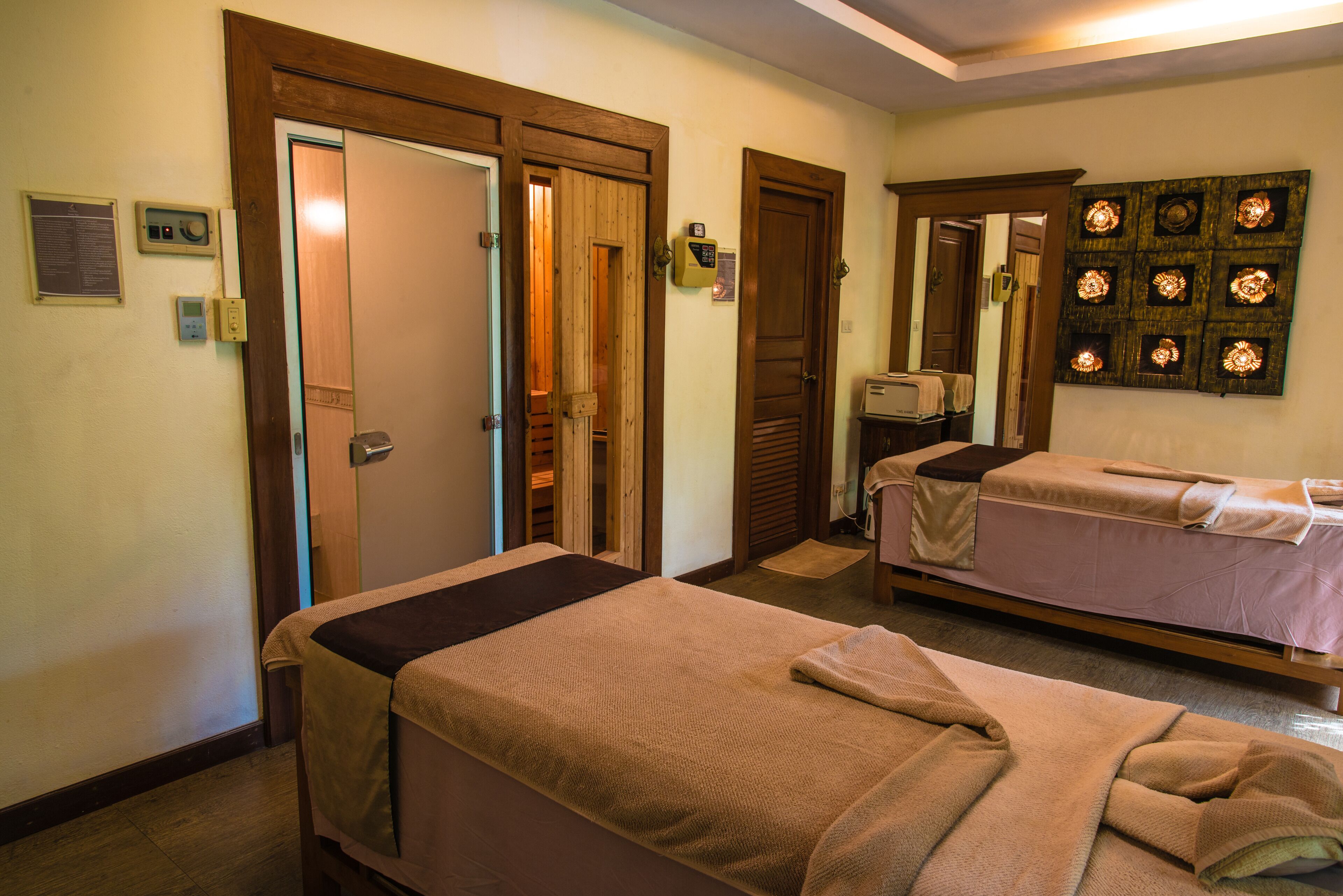 A hotel room with two beds, wooden doors, a small desk, and a wall-mounted light fixture.