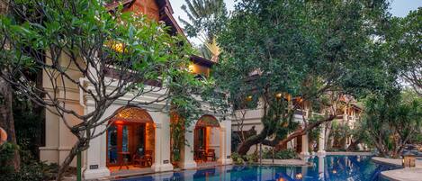 A pool area with a tiled pool, surrounding greenery, and a building with a traditional architectural style.