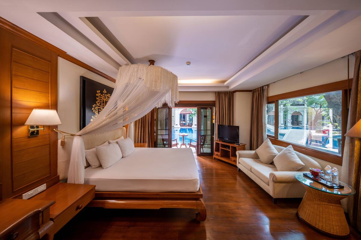 A spacious hotel room with a large bed, a sitting area with a sofa, a television, and a view of the outside.