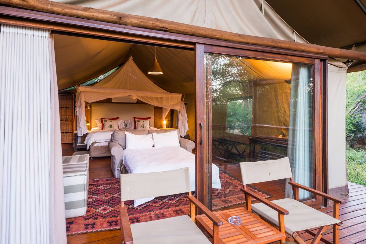 A tented accommodation with a bed, a canopy, and a table with chairs.
