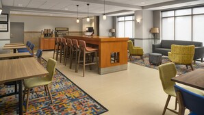 Um lobby moderno de hotel com área de bar, assentos e carpete estampado.