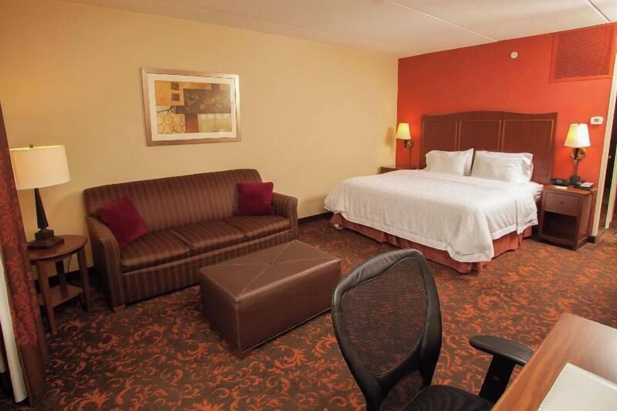 A hotel room with a bed, a sofa, a chair, a small table, and a lamp.