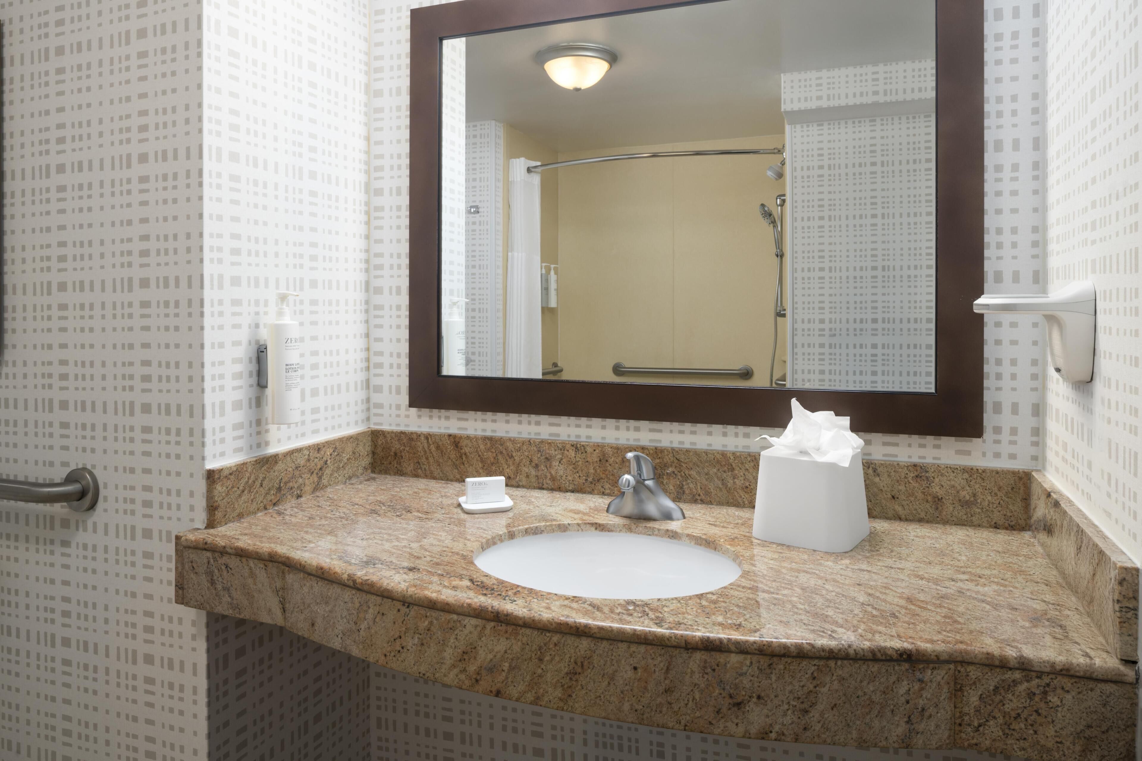 A bathroom with a sink, mirror, and towel dispenser.