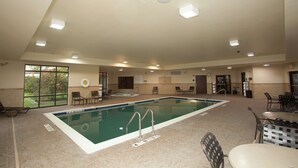 Piscina interior com chão ladrilhado, escada de piscina e várias cadeiras e mesas ao redor da área da piscina.