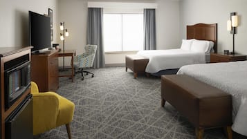 Ein Hotelzimmer mit Bett, Schreibtisch mit Fernseher, Stuhl, Bank und einem Fenster mit Vorhängen.