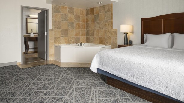 Quarto de hotel com uma cama grande, uma banheira, uma mesa de cabeceira com abajur e um banheiro com espelho e pia.