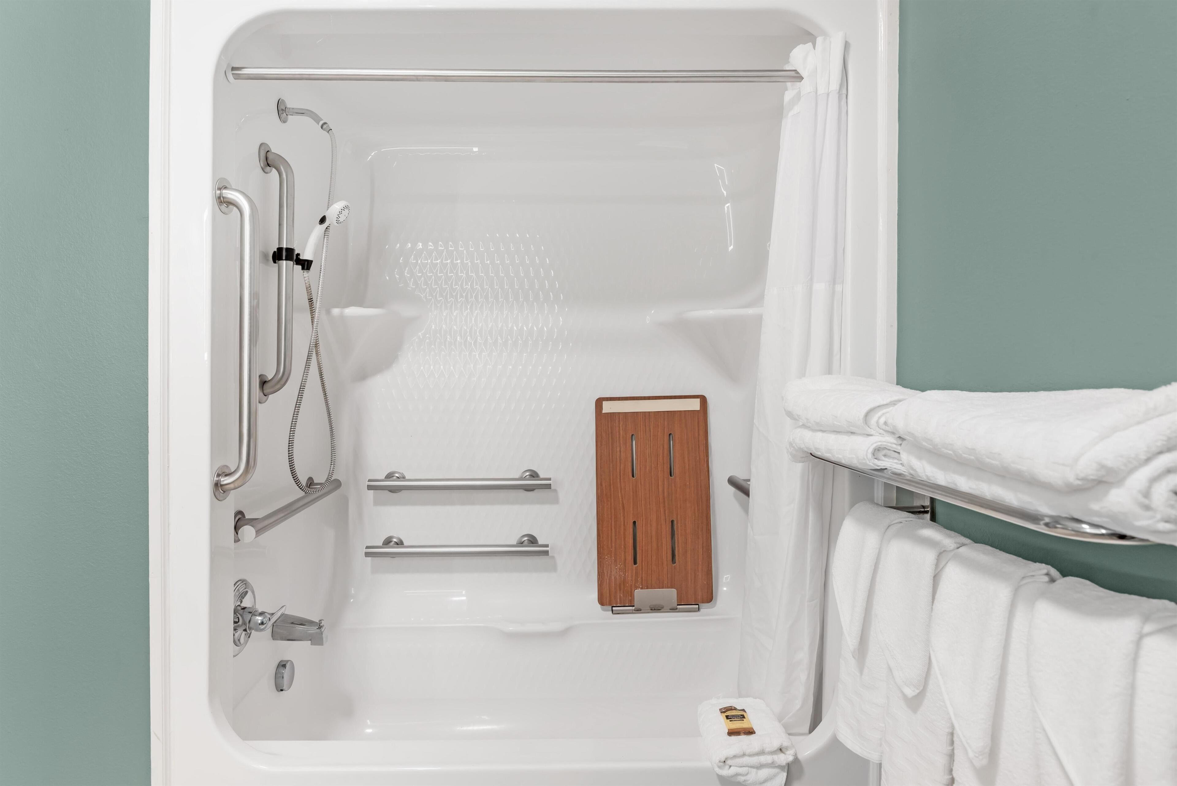 A bathtub with a wooden panel, grab bars, and a towel rack.