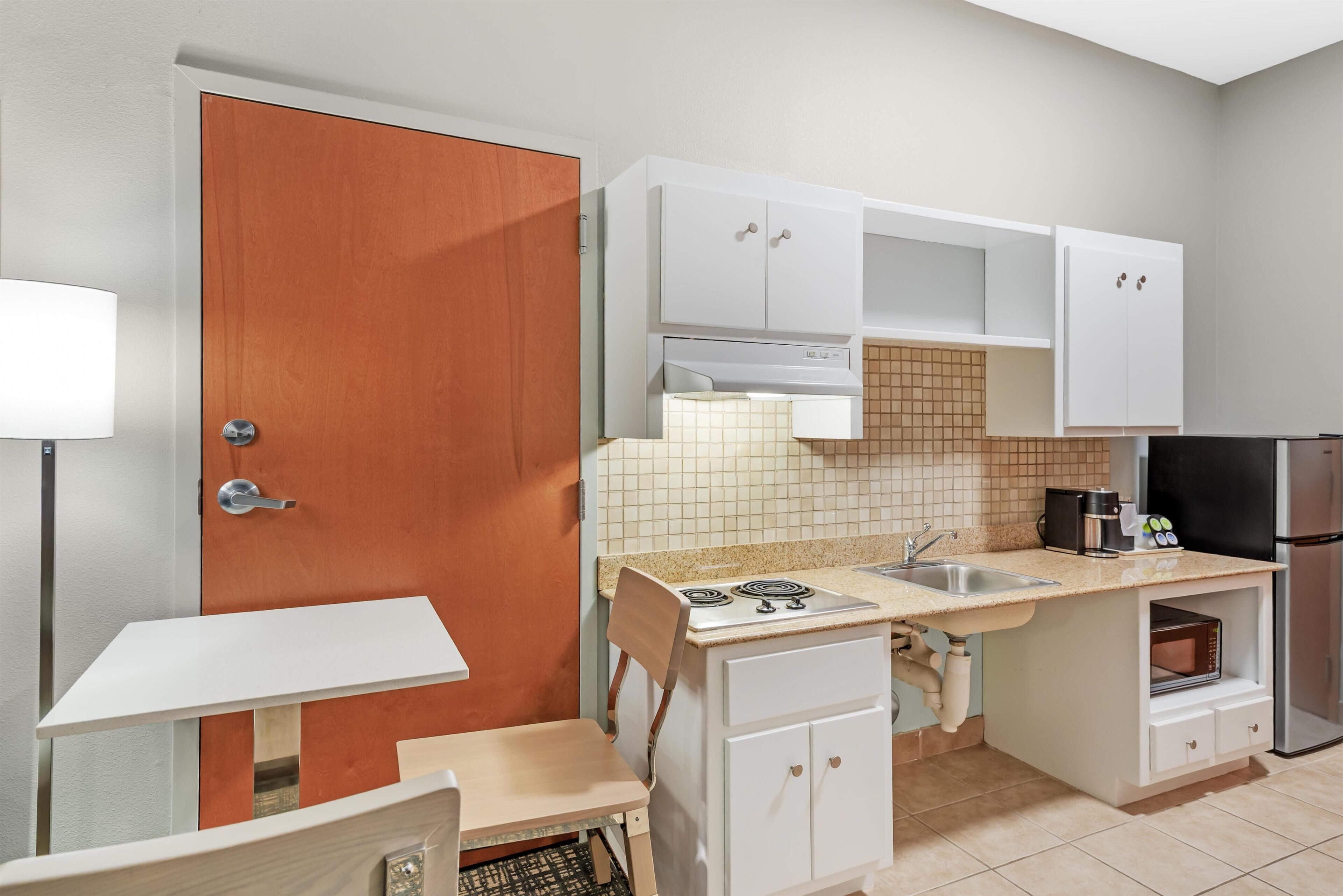 Cocina compacta con puerta de madera, armarios blancos, una encimera, un lavabo, una estufa y un microondas.