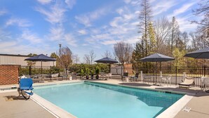 A rectangular swimming pool with a clear blue water surface, surrounded by lounge chairs and umbrellas, and a brick wall in the background. - Best Western Plus Glen Allen Inn (Glen Allen)