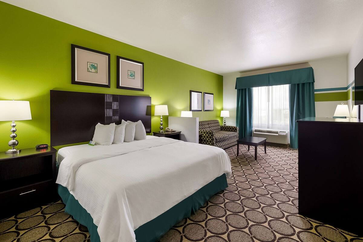 A hotel room with a large bed, two bedside tables with lamps, a chair, a desk, and a large window with curtains.