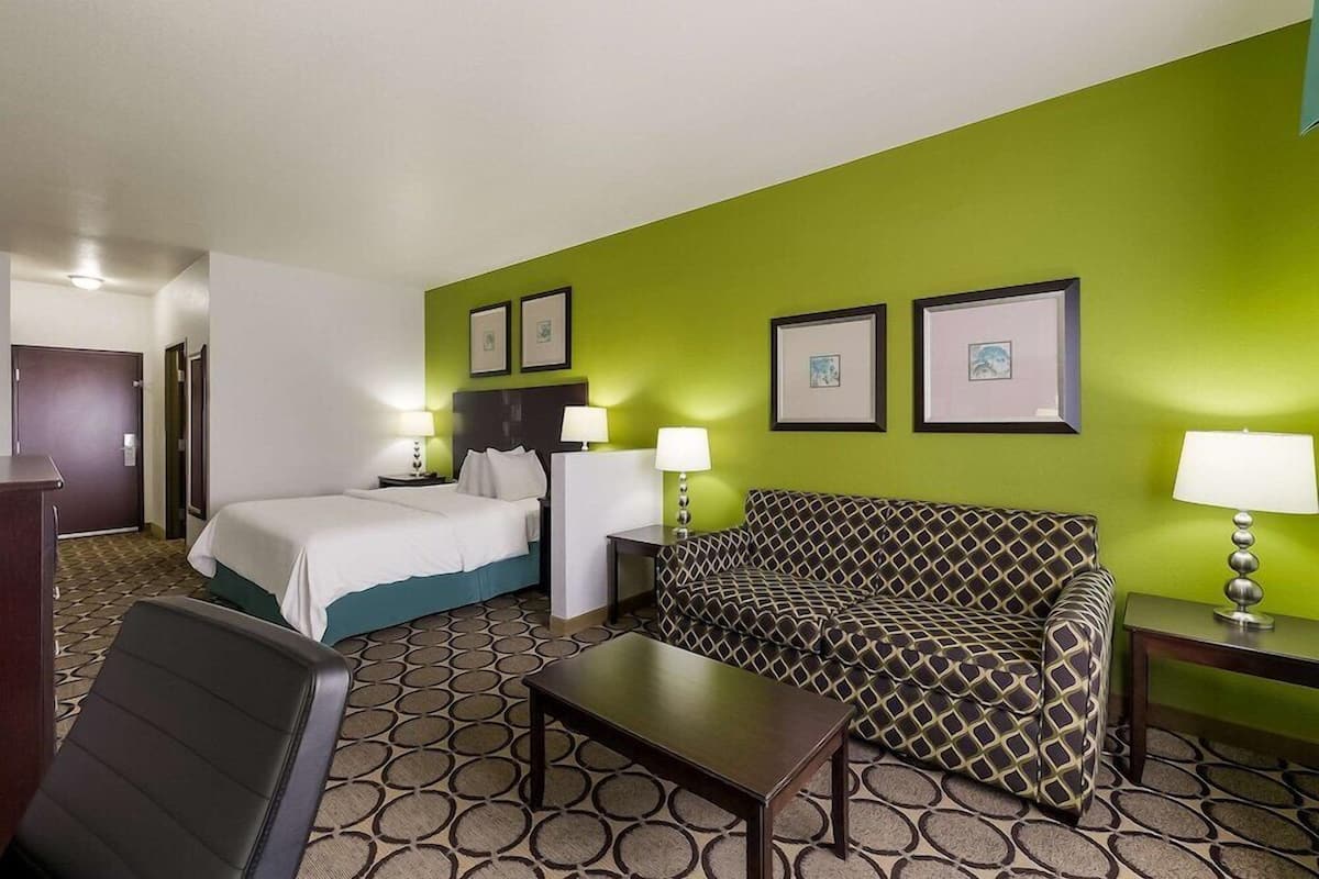 A hotel room with a bed, a sofa, a desk, and two lamps.
