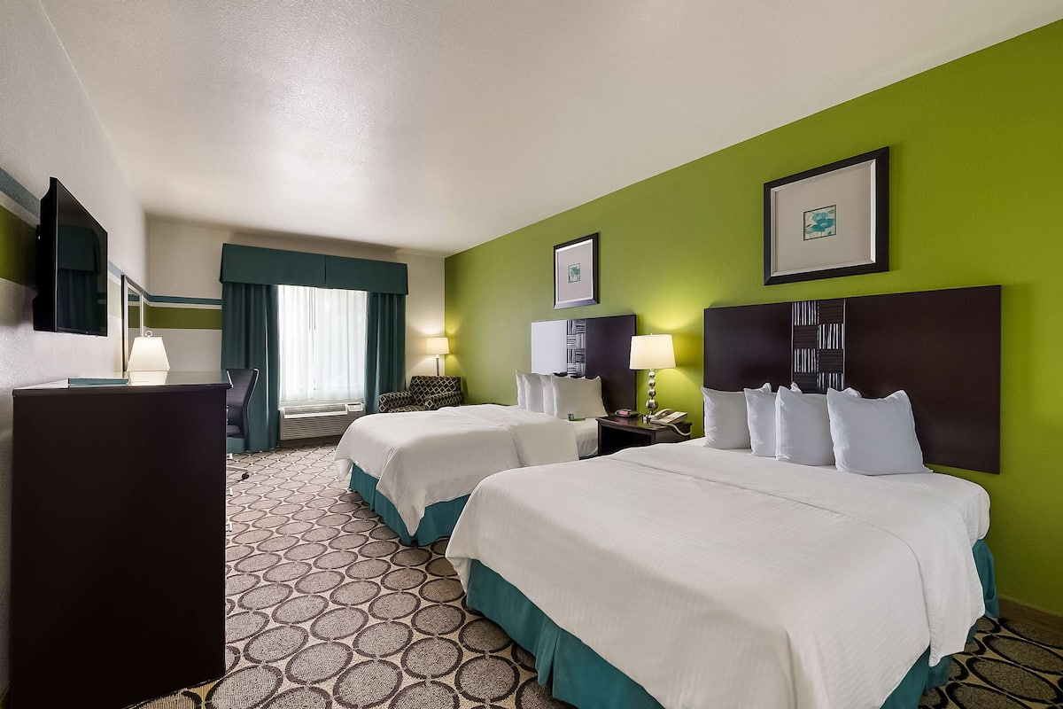 A hotel room with two beds, a desk, a chair, a TV, and a window with curtains.
