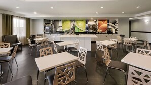 A modern dining area with white tables and chairs, a central island with kitchen appliances, and a large mural on the back wall. - Best Western Douglas Inn & Suites (Douglas)