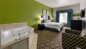 A hotel room with a large bathtub, a bed with a blue headboard, a desk, and a patterned carpet. - Best Western Douglas Inn & Suites (Douglas)