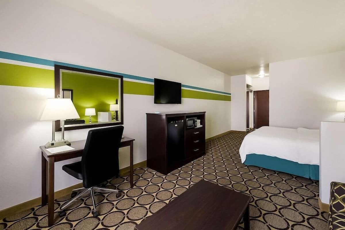 A hotel room with a bed, desk, chair, TV, and a minibar.