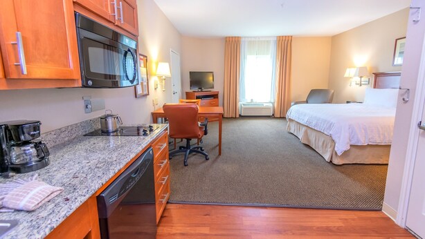 A hotel room with a kitchenette, a bed, a desk, and a chair.