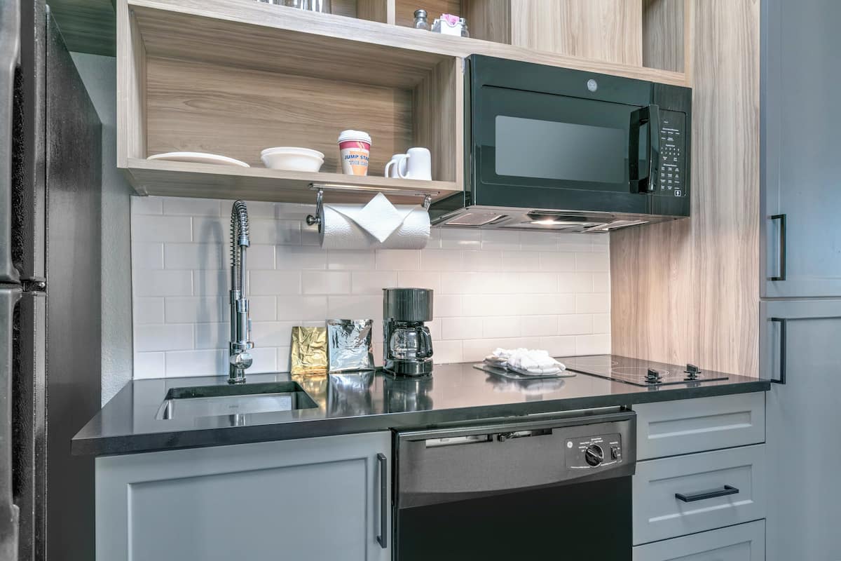A modern kitchen with a black microwave, stainless steel appliances, and wooden cabinetry.