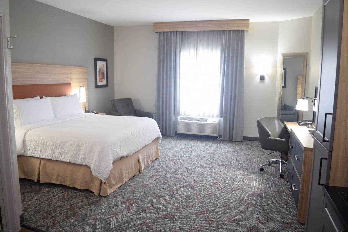 A hotel room with a large bed, a desk with a chair, a desk lamp, and a window with curtains.