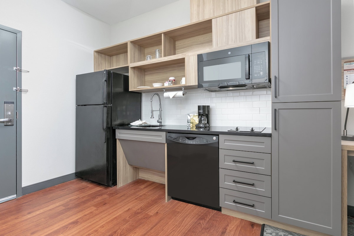A modern kitchen with grey cabinets, a black refrigerator, a microwave, and a dishwasher.