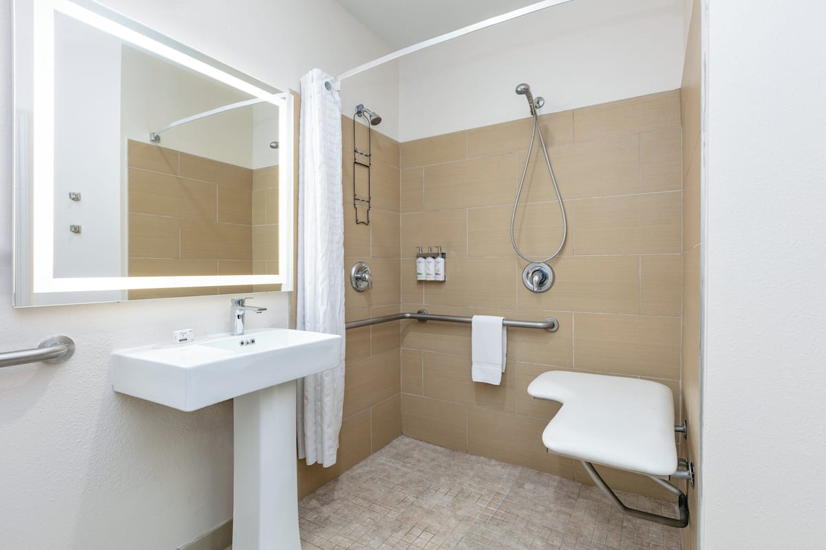A bathroom with a white sink, a mirror, a shower with a grab bar, and a white toilet.